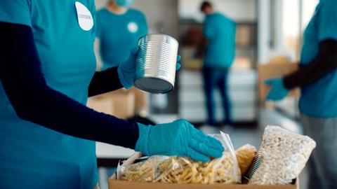 Gloved volunteer placing nonperishible food items into a cardboard box.