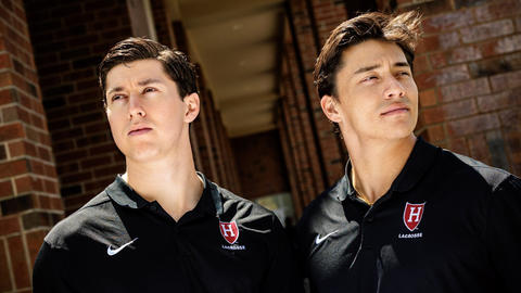 Owen Guest, at left, and Francisco Cortes standing shoulder to shoulder in black Harvard Lacrosse polos, each looking to the distance.
