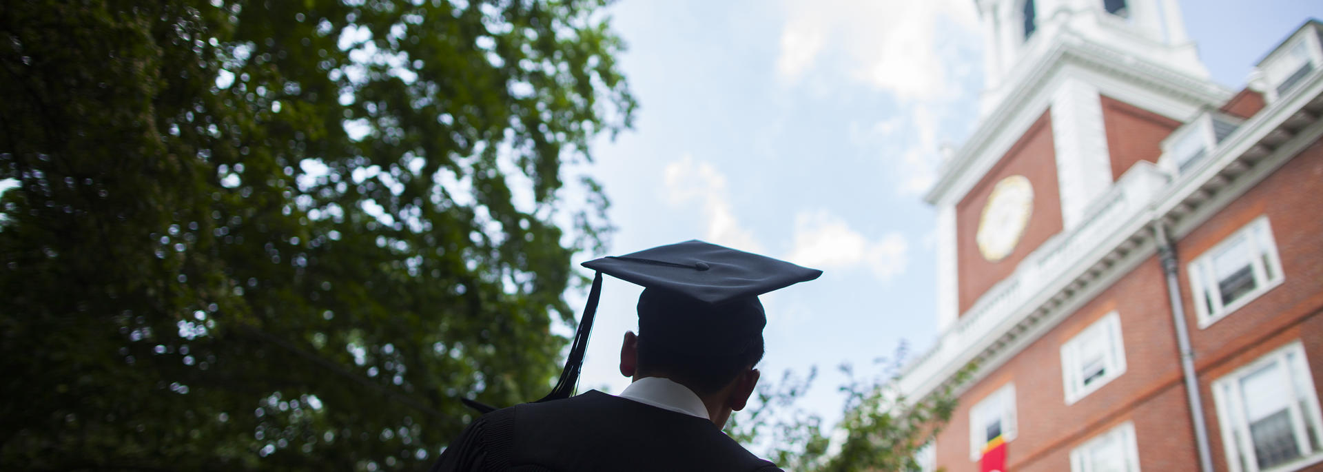 A graduate in a cap and gown stands in Harvard Yard.